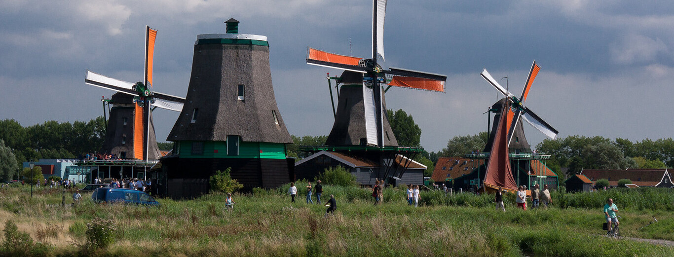 Scenic countryside landscape with four traditional Dutch windmills and people walking and cycling along a path