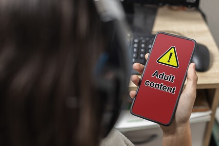 Jovem mexendo em celular com a mensagem "conteúdo adulto" na tela. Créditos: ShutterStock