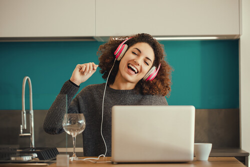 Mulher ouvindo música no notebook de fone de ouvido. Créditos: banco de imagens