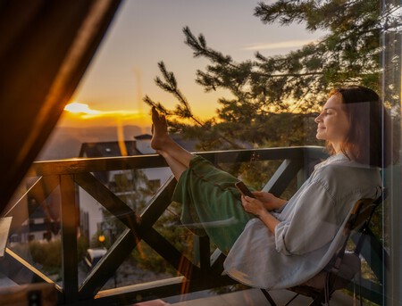 Mulher sentada na varanda observando a vista montanhosa.