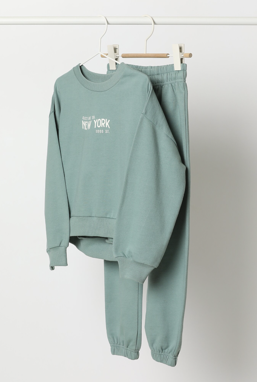 Conjunto de sudadera estampada y pantalón. Sudadera de corte relajado de cuello redondo y puños y bajo acabados en canalé elástico. En la parte delantera cuenta con diferentes estampados de textos. El pantalón en combinación de color está confeccionado en un algodón suave con cintura elástica y cordones de ajuste. El tejido tiene un suave cepillado en el interior, que le aporta sensación de confortabilidad y calidez. Su tejido de algodón elástico facilita el movimiento y lo convierte en un conjunto cómodo para el día a día y actividades deportivas o extraescolares.