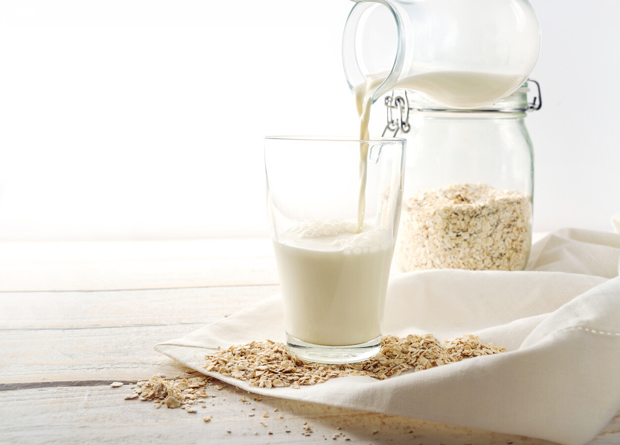 Vaso de leche de avena casera junto a avena en grano sobre una superficie de madera