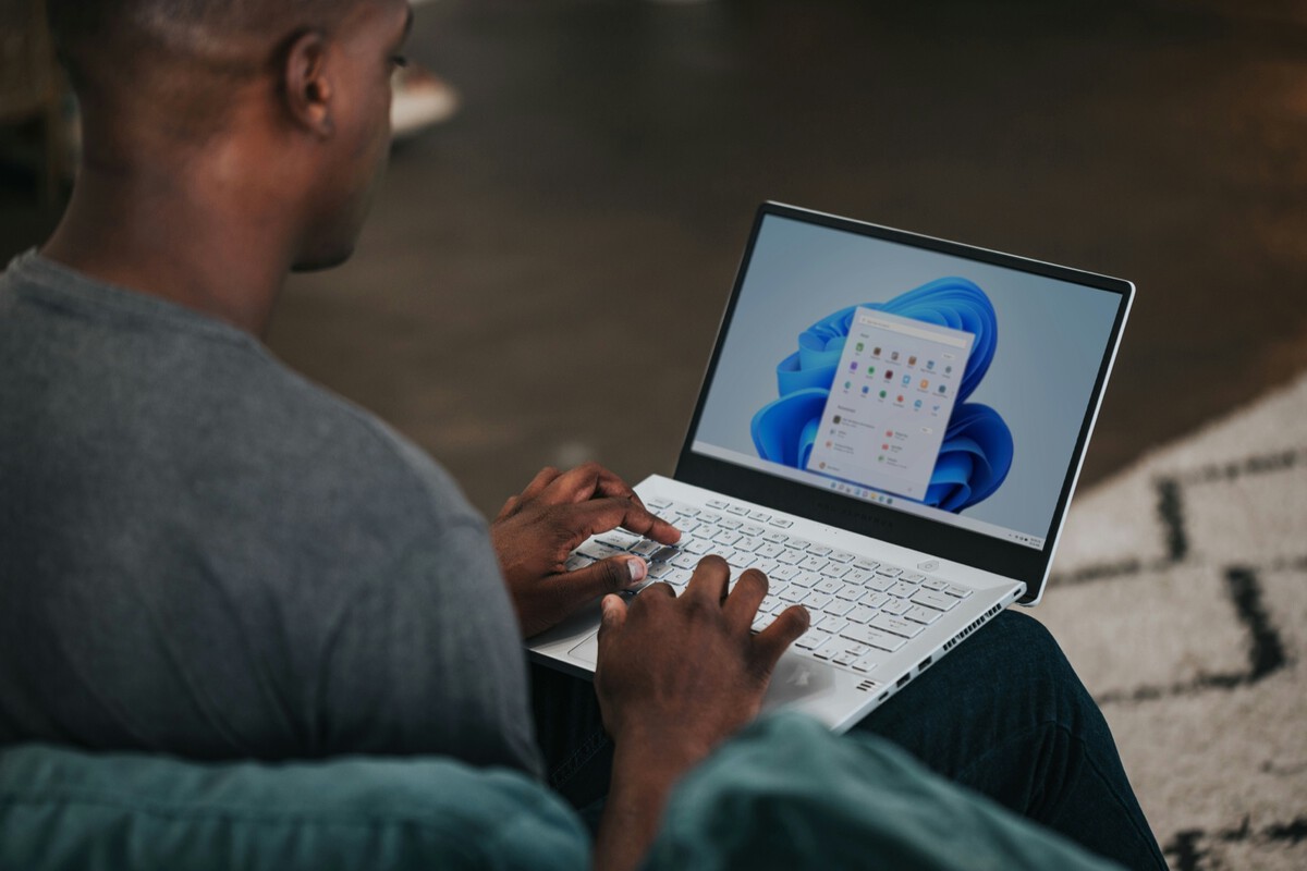 Person typing on a white laptop with Windows 11 Start menu open on screen