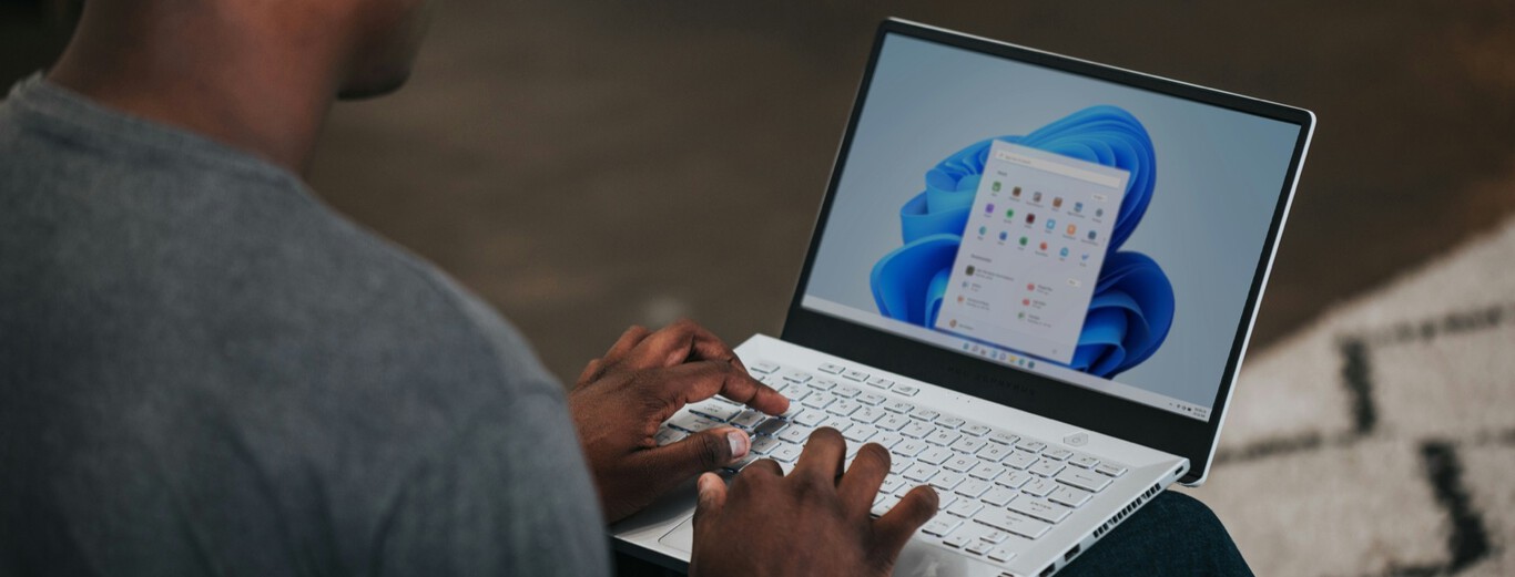 Person typing on keyboard of white laptop showing Windows 11 Start menu