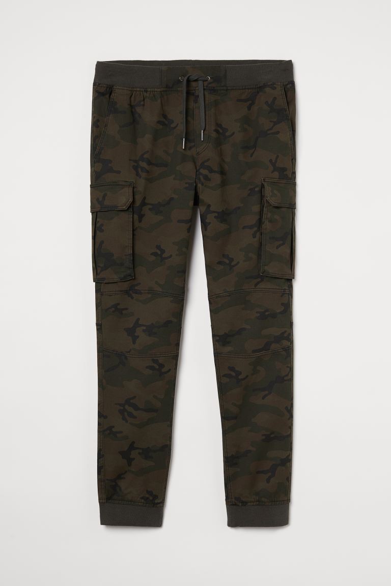 Joggers en sarga de algodón con cintura elástica y cordón de ajuste, bolsillos al bies y bolsillos traseros y en las perneras con solapa y botones de presión ocultos. Perneras pitillo con costuras sobre las rodillas y bajos en punto elástico.