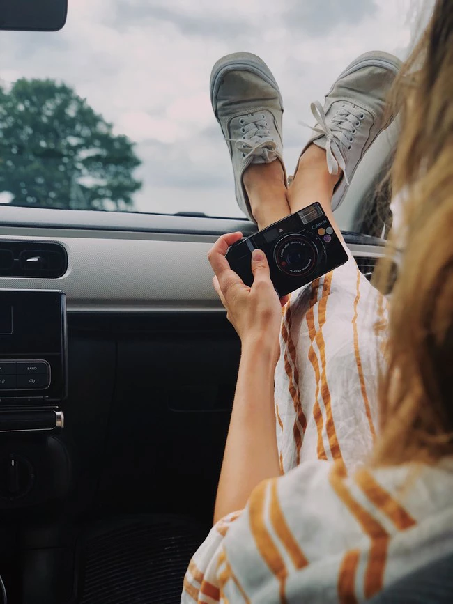 Woman Holding Compact Camera While Feet On Top Of Vehicle 1222469