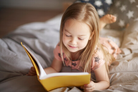 Close Up Portrait Of Little Girl Reading In Bed