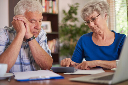 Pareja de personas mayores con cara de preocupación ante una calculadora