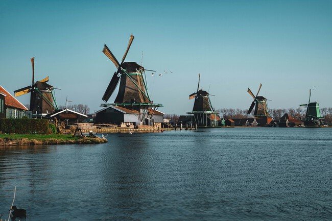 Row of five traditional Dutch windmills along calm water under clear blue sky