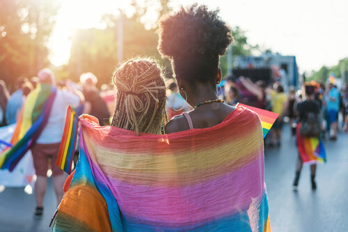 Duas mulheres se abraçando com bandeira LGBTQIA+. Créditos: banco de imagens