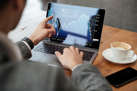 Hombre de negocios con portatil señalando una gráfica bursátil en pantalla
