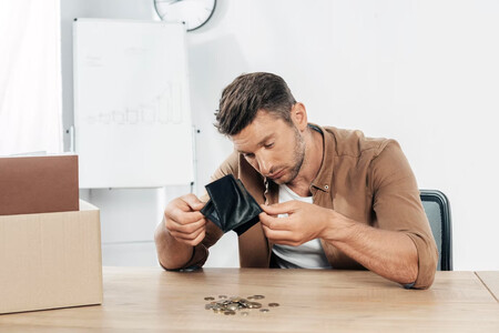 Hombre vaciando su cartera con expresión triste, apenas caen un puñado de monedas