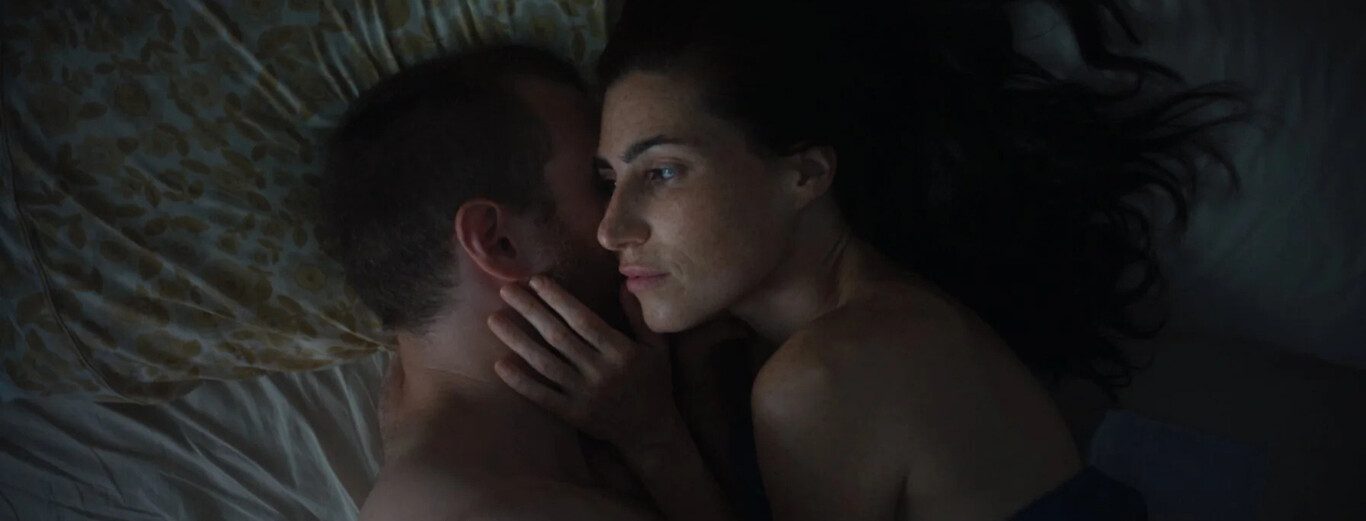 Close-up of a couple lying in bed, the woman looking thoughtful while touching the man's face.