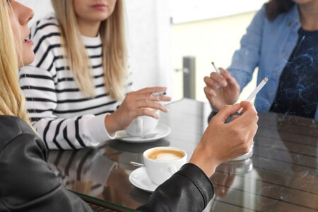 Mulheres sentadas em uma mesa fumando e tomando café.