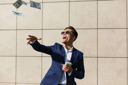 Hombre joven con traje, corbata y gafas de sol arrojando dinero y riendo