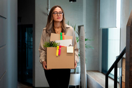 Mujer dejando su trabajo feliz, llevando una caja de cartón con sus pertenencias. Estar dispuesto a dejar el trabajo es fundamental para un ascenso.