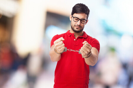 Hombre Esposado, lleva gafas, polo rojo y se mira las esposas