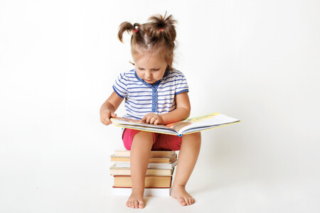 Curious Female Child With Two Funny Pony Tails Sits On Pile Of Books Reads Interesting Faity Tale Views Colourful Pictures With Great Interest Learns To Read Isolated On White Studio 1