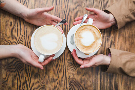 Dos personas tomando café vistas desde arriba, solo se ven las manos y las tazas, son un hombre y una mujer