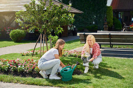 Mother And Daughter In Gloves Planting Flowers At Garden