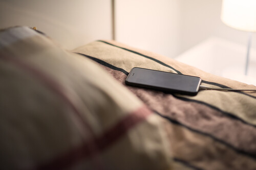 Celular carregando em cima da cama. Créditos:	spyarm//gettyimages