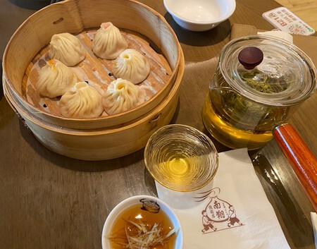 Primer plano de xiaolongbao servidos en vaporera de bambú, acompañado de té.