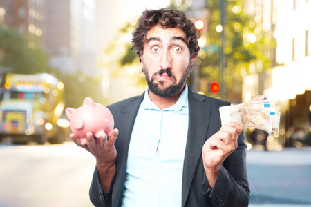Hombre con barba indeciso, en una mano tiene una hucha de cerdito y en la otra, dinero