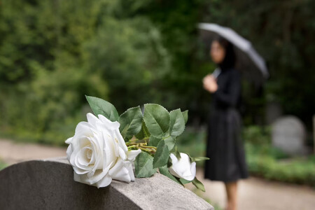 Rosa blanca encima de una lápida, una mujer de luto en segundo plano y borrosa