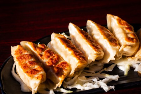 Plato negro con gyozas (dumplings japoneses) dorados servidos encima de una mesa de madera