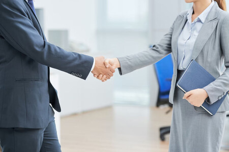 Un hombre y una mujer con traje de negocios dándose la mano tras la negociación de un salario