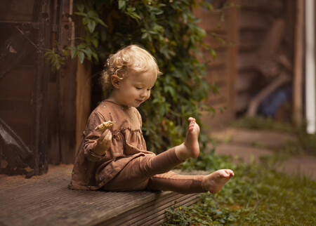 Adorable Child Sitting Barefoot On The Porch While Eating Cookie