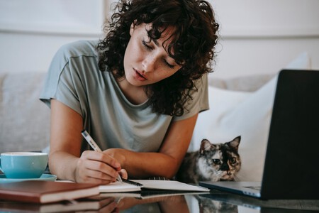 Mujer joven escribe en una libreta al lado de un gato.