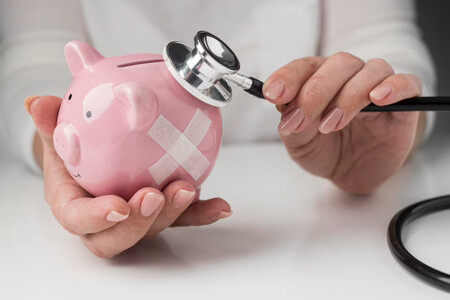 Una hucha de cerdito con una tirita y siendo auscultada por un médico