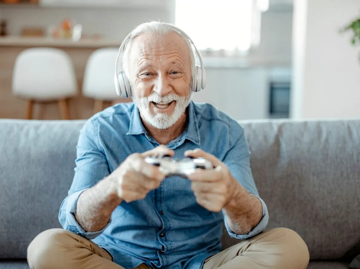 anciano jugando videojuegos, jugador anciano con laptop y auriculares  sonriendo. ilustración conceptual del abuelo de pelo gris sentado en el  sillón y jugando juegos a través de la computadora portátil. 5149594 Vector, image size:1200x899