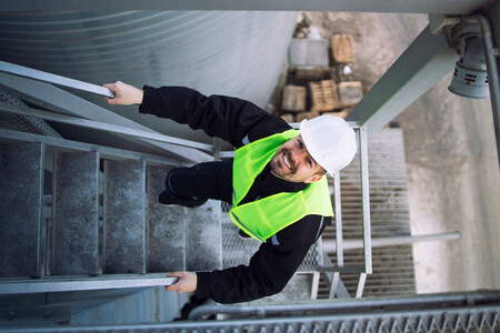 Obrero de la construcción sonriente subiendo una escalera y mirando a cámara