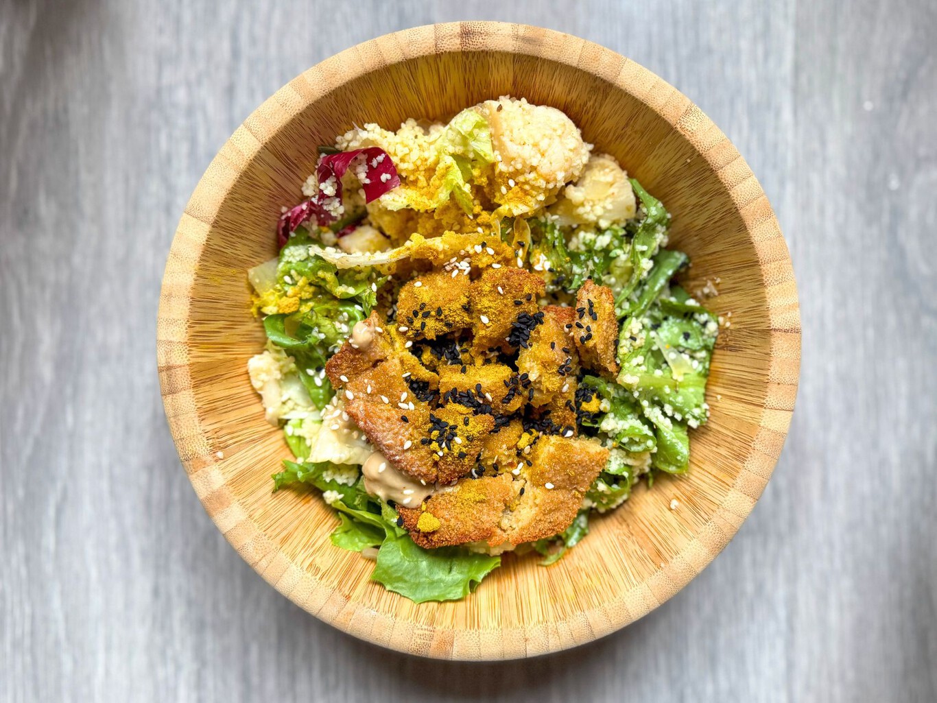 Ensalada con base de cereales, hojas verdes, vegetales y milanesa vegetal en un plato informal