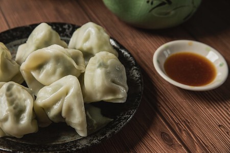 Plato de comida con jiaozi (dumplings) servidos en un bol, acompañado de pasta y salsa, con palillos a un lado, presentados sobre una mesa