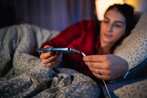 mulher colocando celular para carregar em cima da cama