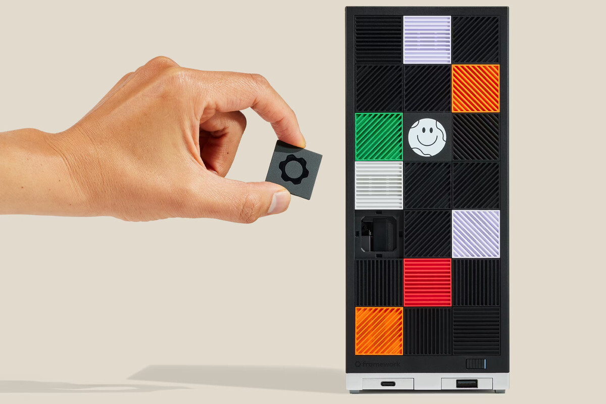 Hand holding a small square piece with a gear symbol above a panel covered with colorful square tiles, some with smiley faces, part of an electronic device