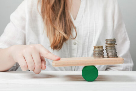 Mujer equilibrando una tabla sobre un rodillo, que tiene monedas en un extremo y su dedo en otro equilibrando