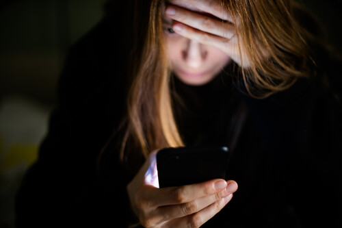 Menina mexendo no celular com mão na cabeça. Créditos:Photographer, Basak Gurbuz Derman/GettyImages