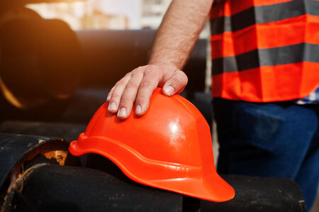Casco de obrero en primer plano, una mano se apoya sobre él