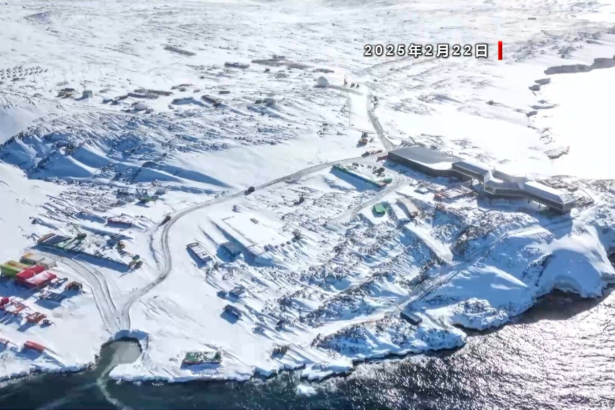 Aerial view of snowy coastal Antarctic area with modern building near shoreline and scattered structures.