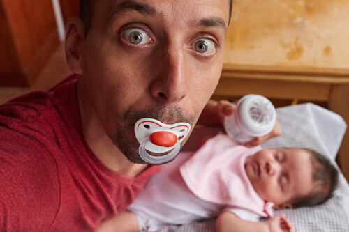 Homem chupando chupeta com bebê na frente. Créditos: banco de imagens