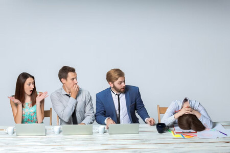 Mujer sentada en el trabajo al lado de tres compañeros tóxicos que la desmoralizan hasta acabar derrotada