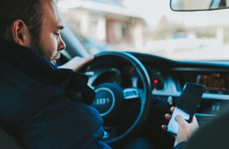 Conductor sujetando el teléfono móvil con la mano en el coche