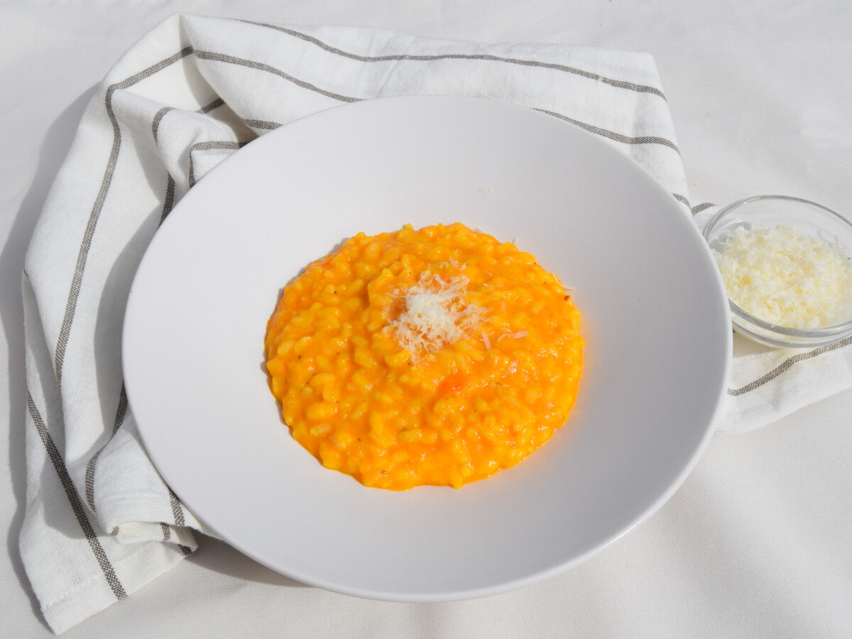 Plato de risotto de zanahoria cremoso con queso parmesano rallado