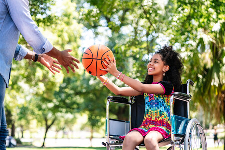Little Girl In Wheelchair Having Fun With Her Father While Playing Basketball Together At Park