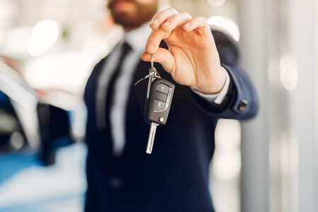 Un vendedor de coche extendiendo una llave de un vehículo nuevo