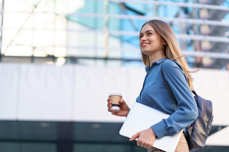Mujer Exitosa laboralmente, sonriendo con un café en una mano y un portátil bajo el brazo